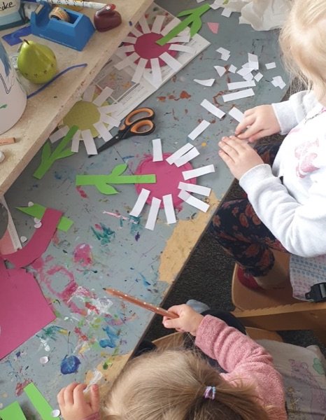 Kinder basteln am Tisch mit Papierblumen und Kleber