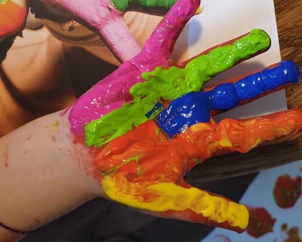 Eine bunt bemalte Kinderhand über einem Bild mit Handabdrücken