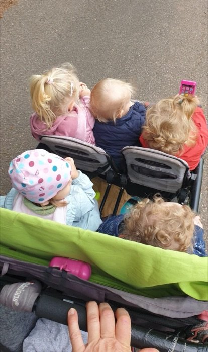 Vier Kinder sitzen im großen Kinderwagen, von hinten fotografiert.