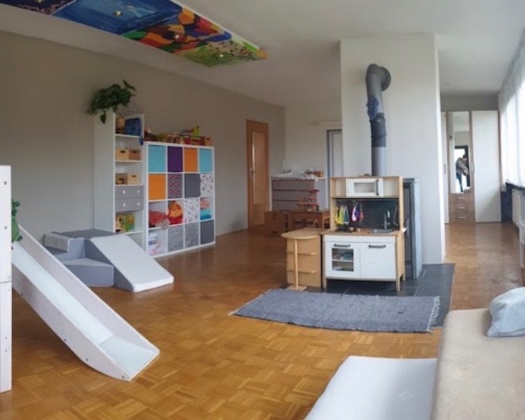 Das helle Kinderzimmer mit Hochbett und Rutsche, Spielregal, Kinderküche und Teppich auf Parkettboden.