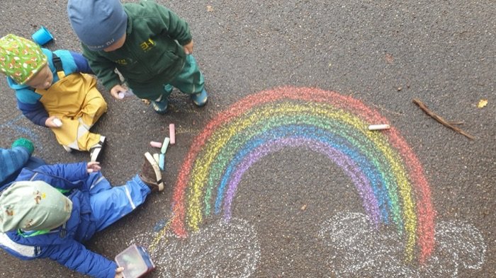 Kinder malen mit Straßenkreide einen großen Regenbogen.