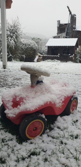 Ein Bobbycar im Schnee im Garten.